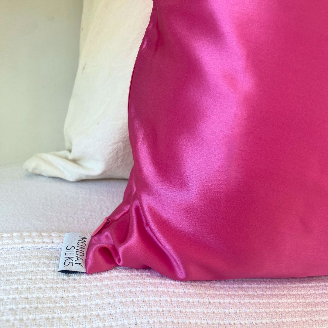 Close-up of fuchsia silk pillowcase with Monday Silks NZ label, emphasizing lustrous finish and elegant bedding design.