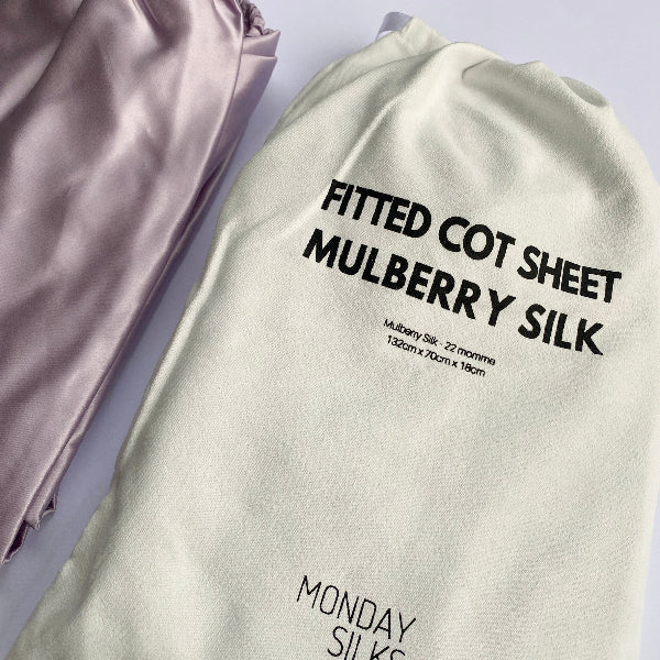 A fitted mulberry silk cot sheet in lilac color displayed on a cot, with the brand name 'Monday Silks' visible on the sheet.