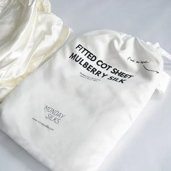 White mulberry silk fitted cot sheet in a branded drawstring storage bag.
