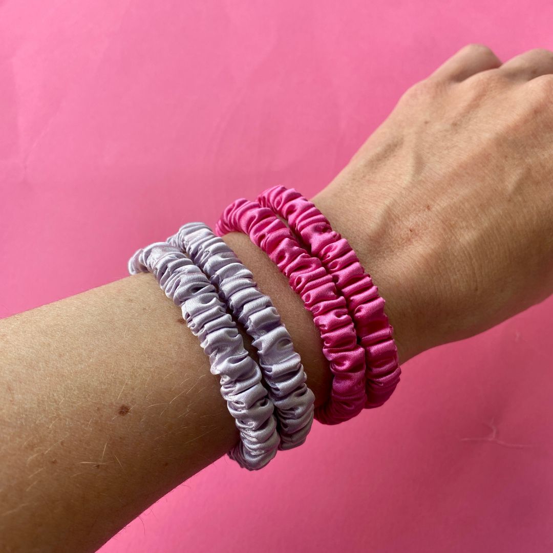 Skinny Silk Scrunchies - 4 Pack (2 x Fuchsia, 2 x Lilac) shown on wrist, highlighting smooth silk texture and vibrant colors for hair care.