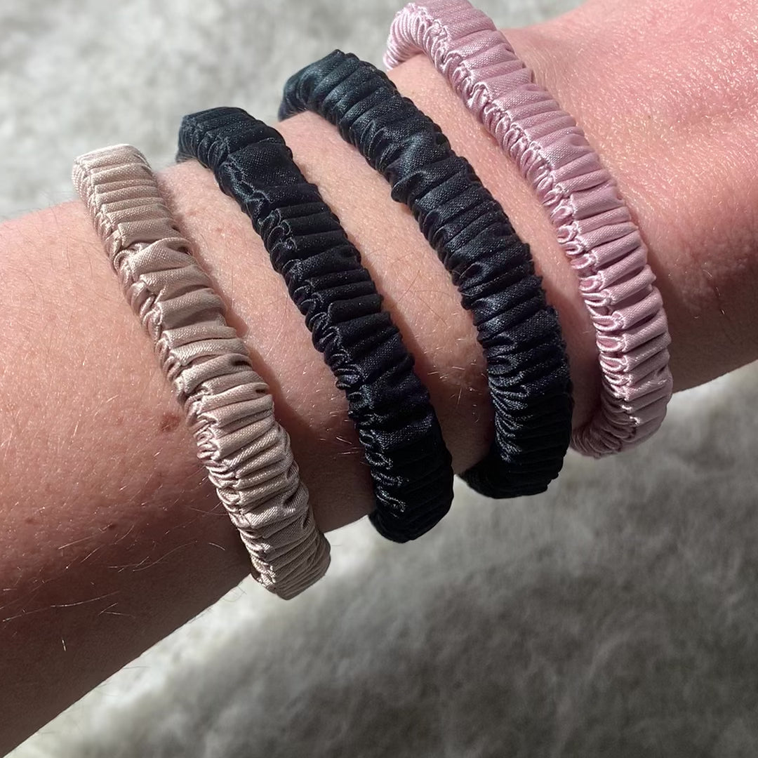 Skinny silk scrunchies on womens wrist to show size. Black pink and champagne skinny silk scrunchies.
